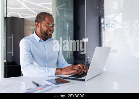 Successful african american businessman working inside office with laptop, man smiling and happy with achievement result at workplace. Stock Photo