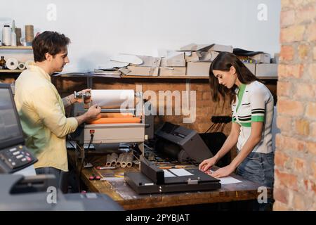 man standing next to flexographic machine and pretty colleague in print center,stock image Stock Photo