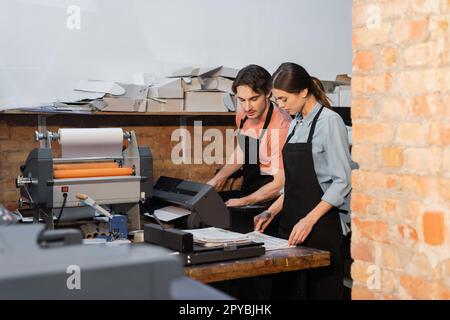 typographers in aprons looking at newspapers while working in print center,stock image Stock Photo