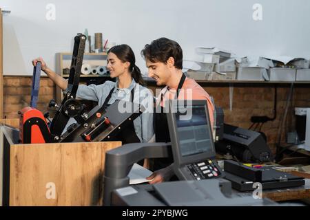 cheerful man and woman in aprons using professional print plotter while working together in print center,stock image Stock Photo