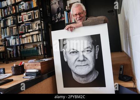 PRODUCTION - 03 May 2023, North Rhine-Westphalia, Königswinter: Portrait photographer Konrad Rufus Müller sits in his living room with a portrait of Chancellor Scholz. Konrad R. Müller has photographed all German chancellors since Adenauer. Photo: Oliver Berg/dpa - ATTENTION: Only for editorial use and only with full mention of the above credit Stock Photo