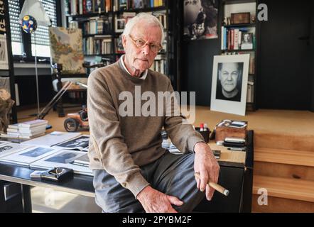 PRODUCTION - 03 May 2023, North Rhine-Westphalia, Königswinter: Portrait photographer Konrad Rufus Müller sits in his living room with a portrait of Chancellor Scholz. Konrad R. Müller has photographed all German chancellors since Adenauer. Photo: Oliver Berg/dpa Stock Photo