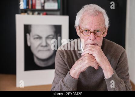 PRODUCTION - 03 May 2023, North Rhine-Westphalia, Königswinter: Portrait photographer Konrad Rufus Müller sits in his living room in front of a portrait of Chancellor Scholz. Konrad R. Müller has photographed all German chancellors since Adenauer. Photo: Oliver Berg/dpa Stock Photo