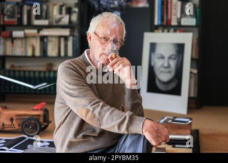 PRODUCTION - 03 May 2023, North Rhine-Westphalia, Königswinter: Portrait photographer Konrad Rufus Müller sits in his living room with a portrait of Chancellor Scholz. Konrad R. Müller has photographed all German chancellors since Adenauer. Photo: Oliver Berg/dpa Stock Photo