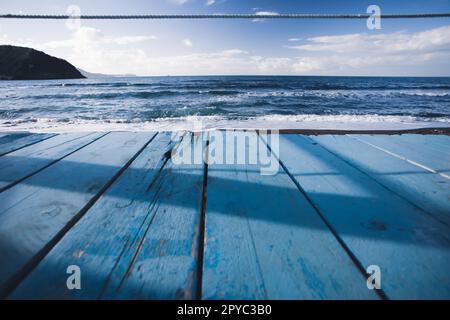 Wooden perspective on blue water shore and blue sky at coast Stock Photo
