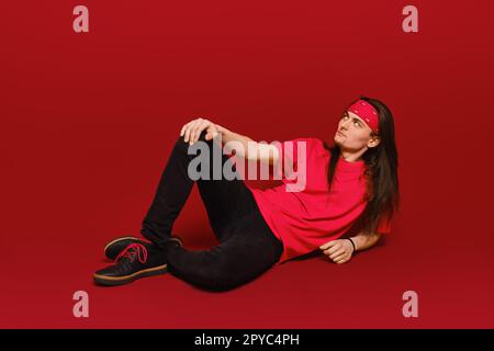 Man with long hair sitting on floor in red studio Stock Photo