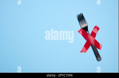 A plastic fork is attached with red adhesive tape on a blue background, a concept of refusing plastic tableware and recycling materials, zero waste Stock Photo