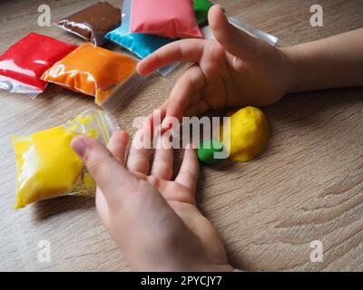 Children's hands crumple soft plasticine. Packages with plasticine are on the table. Creativity for the development of fine motor skills of hands. Creating a mold or model from plasticine Stock Photo