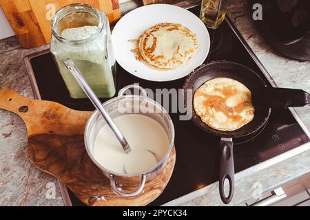 Making thin pancakes on frying pan in kitchen, with cooking dough for crepes and pancakes Stock Photo