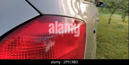 Detail of the rear end of a silver car with focus on the brake lights. Red rear light of the car. Brake signal for the driver driving behind Stock Photo