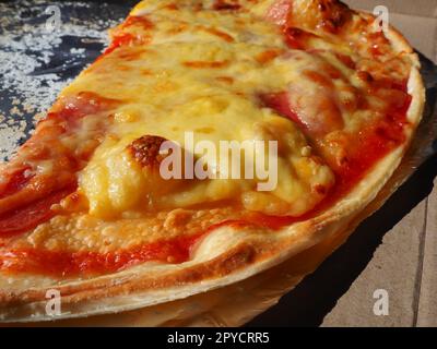 Pizza with tomatoes and cheese in a cardboard box and aluminum foil. Delicious pizza close up. Courier delivery of food to your home. Ordering pizza. Traditional Italian round yeast cake with filling Stock Photo