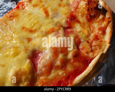 Pizza with tomatoes and cheese in a cardboard box and aluminum foil. Delicious pizza close up. Courier delivery of food to your home. Ordering pizza. Traditional Italian round yeast cake with filling Stock Photo