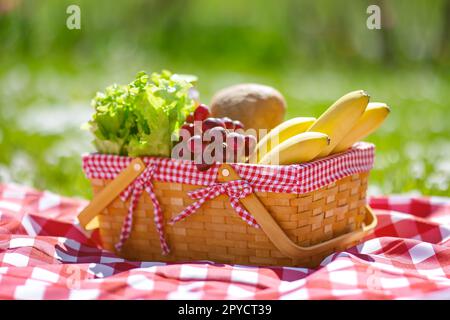 Wicker basket with food standing on the picnic blanket in nature. Stock Photo