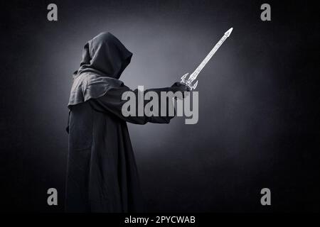 Dark knight with hooded cape and medieval sword over dark misty background Stock Photo