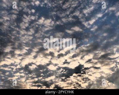 Clouds in the evening sky. The sun's rays pierce the clouds. Blue, yellow and orange colors of the sky and clouds. Beautiful landscape. The sun goes down