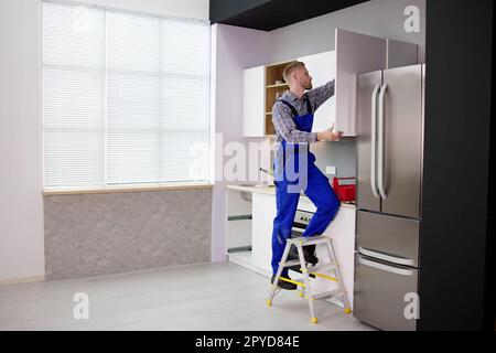 Male Carpenter Assembling White Cabinet On Wall Stock Photo