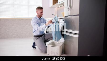 Young Man Loading Clothes Into Washing Machine Stock Photo