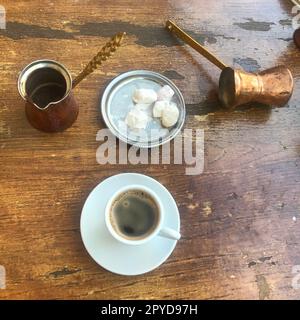 Traditional Greek coffee set on a wooden table next to copper coffee pots with a bowl of sugar cubes and an espresso cup Stock Photo