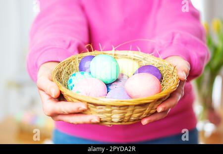 Close up of colorful Easter eggs in a basket. Female hands holding basket with colored Easter eggs. Stock Photo