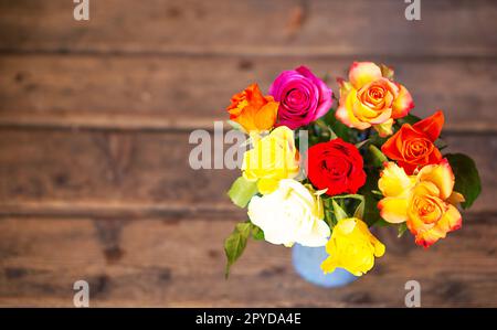 Colorful roses boquet in a blue vase on the old wooden background. Top view, copy space. Stock Photo