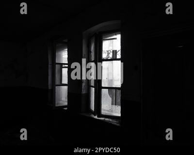 Scary windows. Inside an abandoned house. View of broken windows without a curtain. Grunge scene. Light shines through old wooden frames with broken glass. The concept of abandonment and uselessness Stock Photo