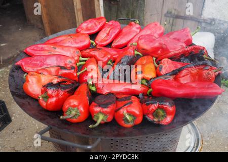 Roasting red peppers for a smoky flavor and quick peeling. Thermal processing of the pepper crop on a metal circle. Brazier container used to burn charcoal fuel for cooking, heating or cultural ritual Stock Photo