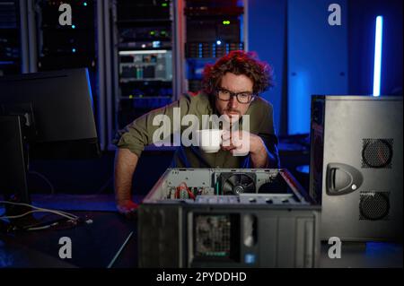 Repairman with cup of coffee looking at disassembled computer system unit Stock Photo