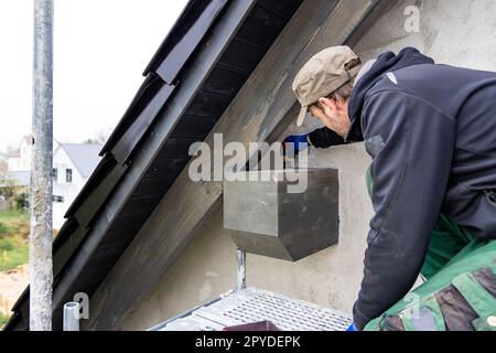 Craftsman applying wood stain to a roof beam on the exterior of a house Stock Photo