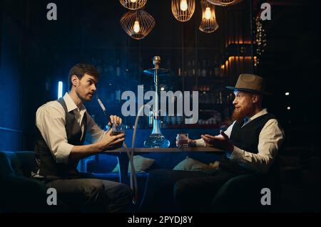 Guys having serious conversation while sitting face to face at hookah bar Stock Photo