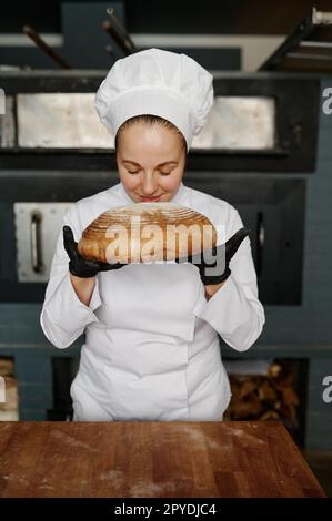 Young female baker smelling fresh bread over modern bakery background Stock Photo