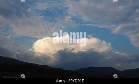 Clouds in the evening sky. The sun's rays pierce the clouds. Blue, yellow and gray colors of the sky and clouds. Beautiful landscape. The sun goes down. Storm weather forecast. Cumulus clouds Stock Photo