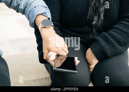 Two Spanish-Latin women with smartphones and smartwatches, selective focus on the clipped hands. Stock Photo