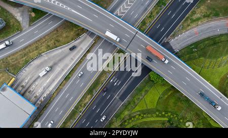 Aerial top view of highway junction interchange road. Drone view of the elevated road, traffic junctions, and green garden. Transport trucks and cars driving on highway. Infrastructure in modern city. Stock Photo