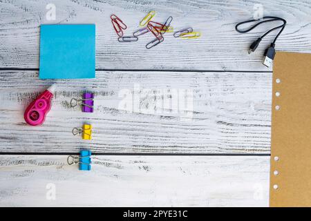 Blue sheets for notes, colored paper clips, a sheet of craft paper, paper clips, a charger for gadgets and a corrector for office work and school on a Stock Photo