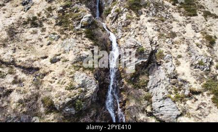 Small waterfall in the middle of an autumnal mountain landscape surrounded by rocks and steep terrain Stock Photo