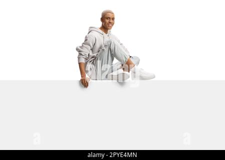 African american gen z guy with bleached hair sitting on a blank panel isolated on white background Stock Photo