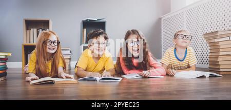 Four cute children in glasses lying on the floor indoors with books Stock Photo