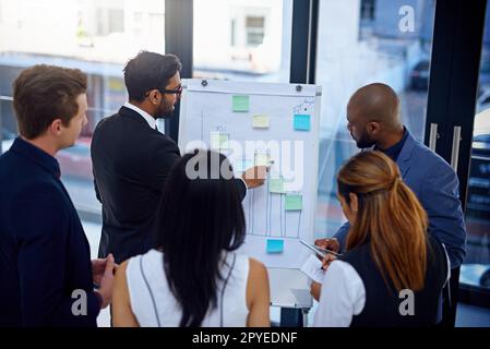 Hes explaining the reason for the decline in numbers lately. a young businessman giving a demonstration on a white board to his colleagues in a modern office. Stock Photo