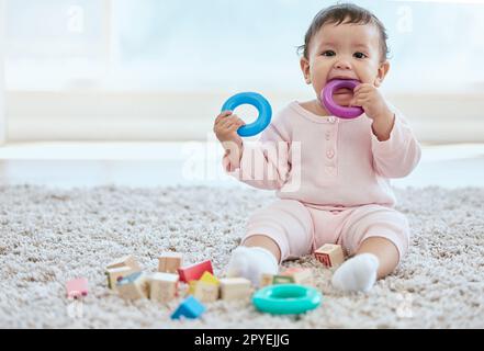 Everything goes in my mouth. an adorable baby girl sitting on the floor at home. Stock Photo