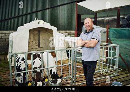 These young ones need a lot of milk. Cropped portrait of a male farmer feeding the calves on his dairy farm. Stock Photo