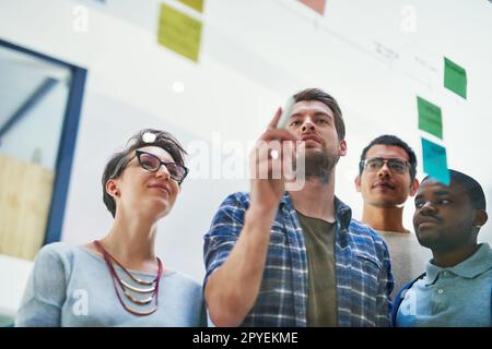 Perhaps we should combine plans. a group of designers brainstorming with notes on a glass wall in an office. Stock Photo