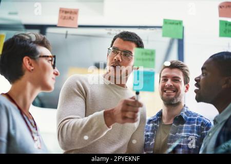 Putting big plans into place. a group of designers brainstorming with notes on a glass wall in an office. Stock Photo