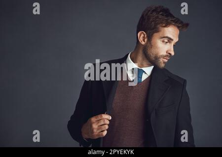 He knows what looks good on him. Studio shot of a stylishly dressed young man posing against a gray background. Stock Photo