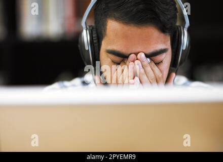I seriously have to take a break. Closeup shot of a stressed out young man working on a computer while listening to music with his eyes closed. Stock Photo