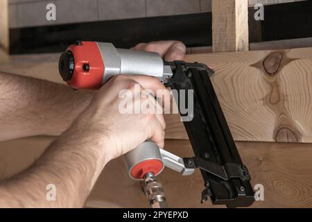 Closeup cropped male hands use pneumatic nailer, stapler nail gun for wooden plank and board. Builder first person view Stock Photo