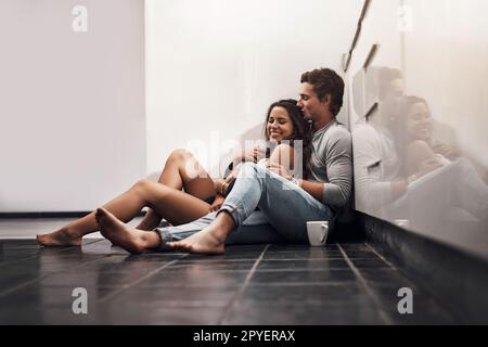 Romance turns a house into paradise. an affectionate young couple sitting on the kitchen floor. Stock Photo