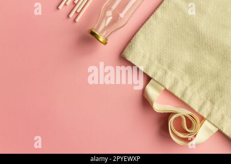 Fabric cotton shopping bags, glass bottles, paper straws and wooden sticks on a pink background. Top view. Copy space. Stock Photo