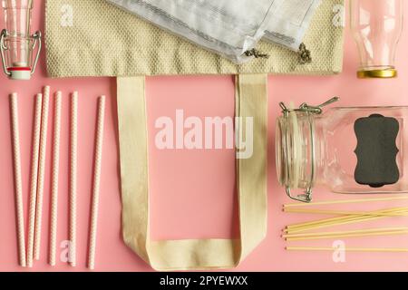 Fabric cotton shopping bags, glass bottles, paper straws and wooden sticks on a pink background. Top view. Copy space. Stock Photo