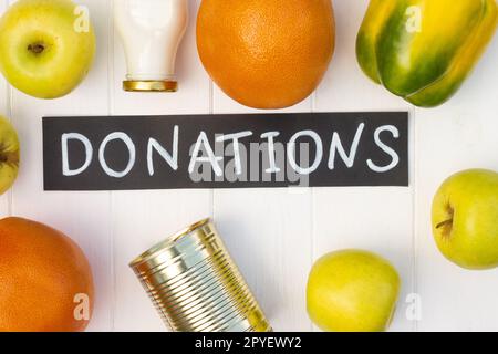 Cereals, canned food, milk, vegetables and fruits with a chalk Donations sign on a white wooden table. Flat lay. Stock Photo