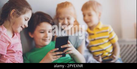 Group of children sitting indoors and looking in the smartphone Stock Photo